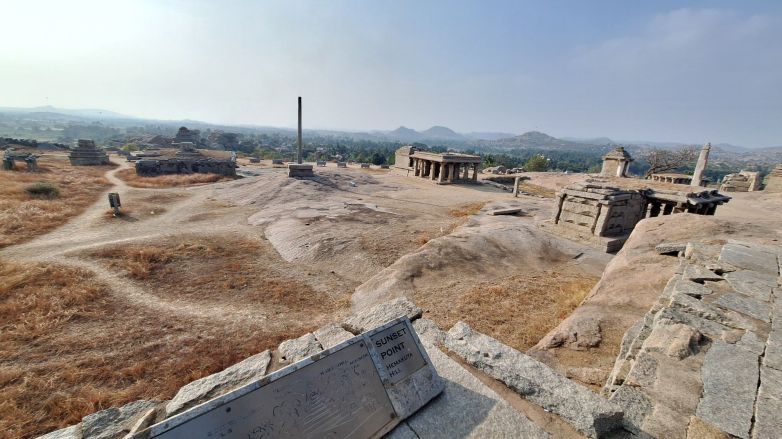 View from Hemakuta Hill at Hampi, Karnataka, India, showing scattered temple ruins across a rocky plateau with mountains visible in the background.